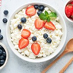 15 Foods to Support Overnight Metabolism and Recovery Cottage cheese topped with strawberries, blueberries, and mint, served with fresh berries and wooden spoons on a light kitchen surface.