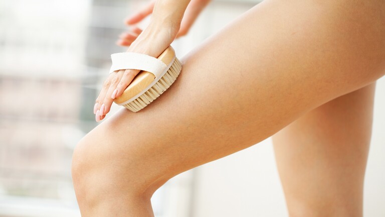 Close-up of a dry brush being used on the thigh during a body care routine.