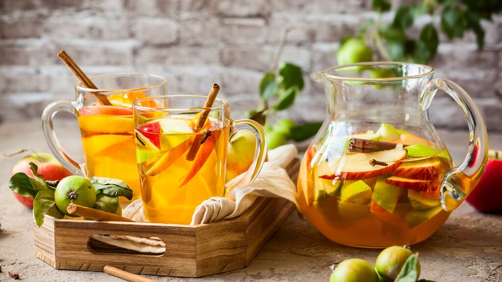 Diluted apple cider vinegar drinks with apple slices and cinnamon sticks served in glass mugs beside a pitcher of infused apple drink.