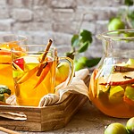 Diluted apple cider vinegar drinks with apple slices and cinnamon sticks served in glass mugs beside a pitcher of infused apple drink.