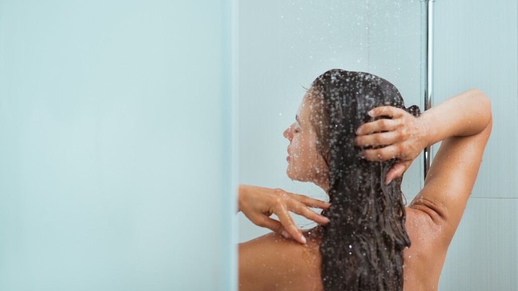 Person rinsing under a shower with water flowing over the shoulders and hair.
