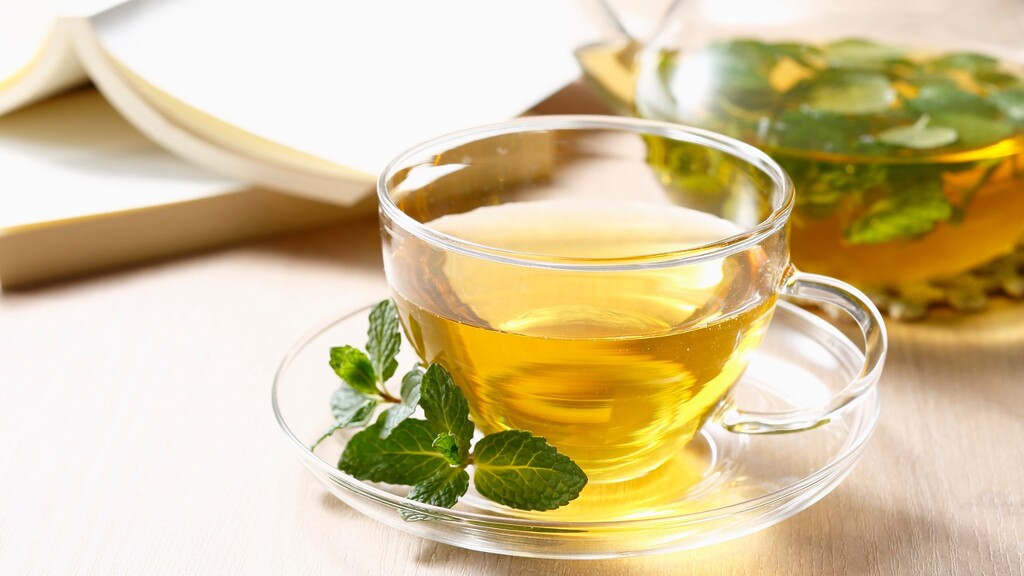 Cup of green tea with fresh mint leaves on a bright table.