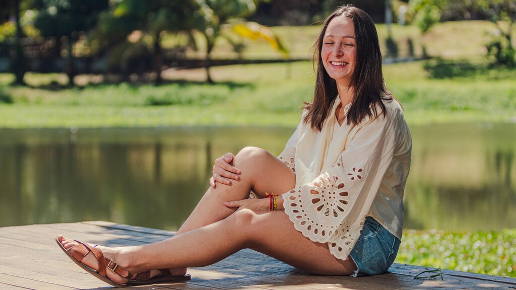 Relaxed woman sitting outdoors by a lake in shorts, comfortable in her skin.