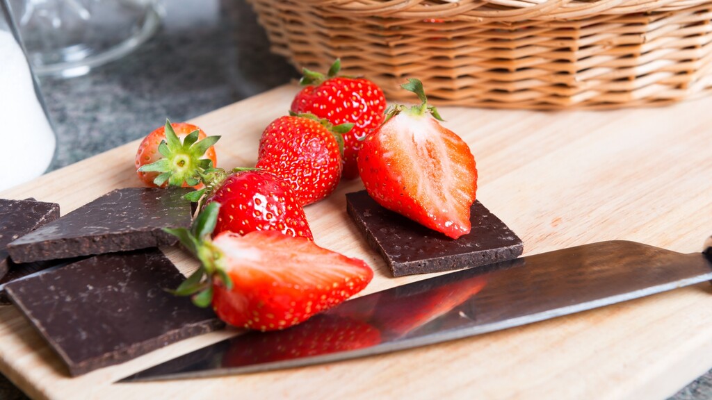 Fresh strawberries and pieces of dark chocolate on a wooden cutting board.
