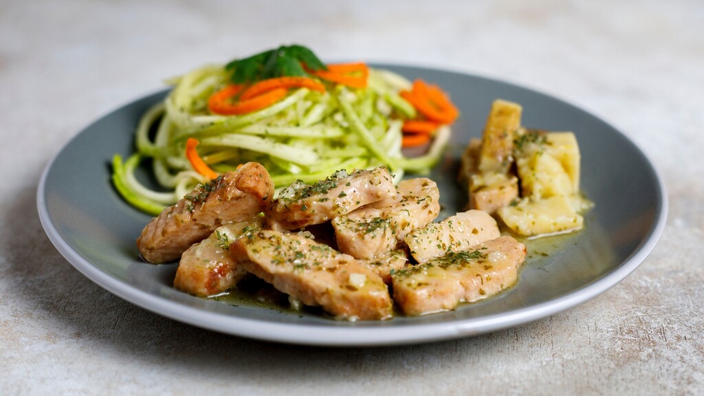 Grilled chicken pieces served with zucchini noodles, carrot ribbons, and roasted potatoes on a gray plate.