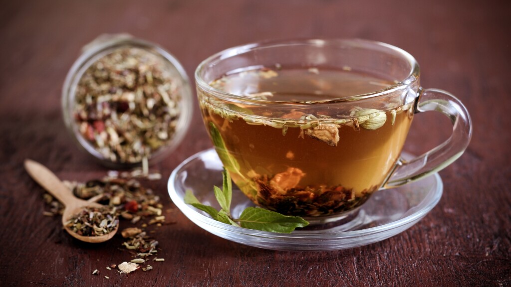 Glass cup of herbal tea with loose dried herbs on a wooden table.