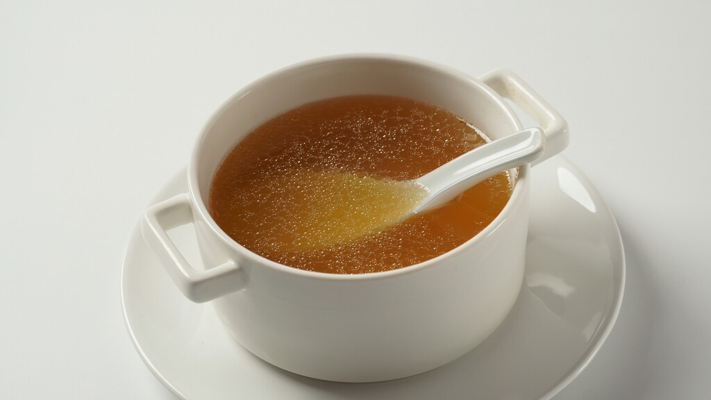 Warm bowl of bone broth served in a white cup with a spoon.