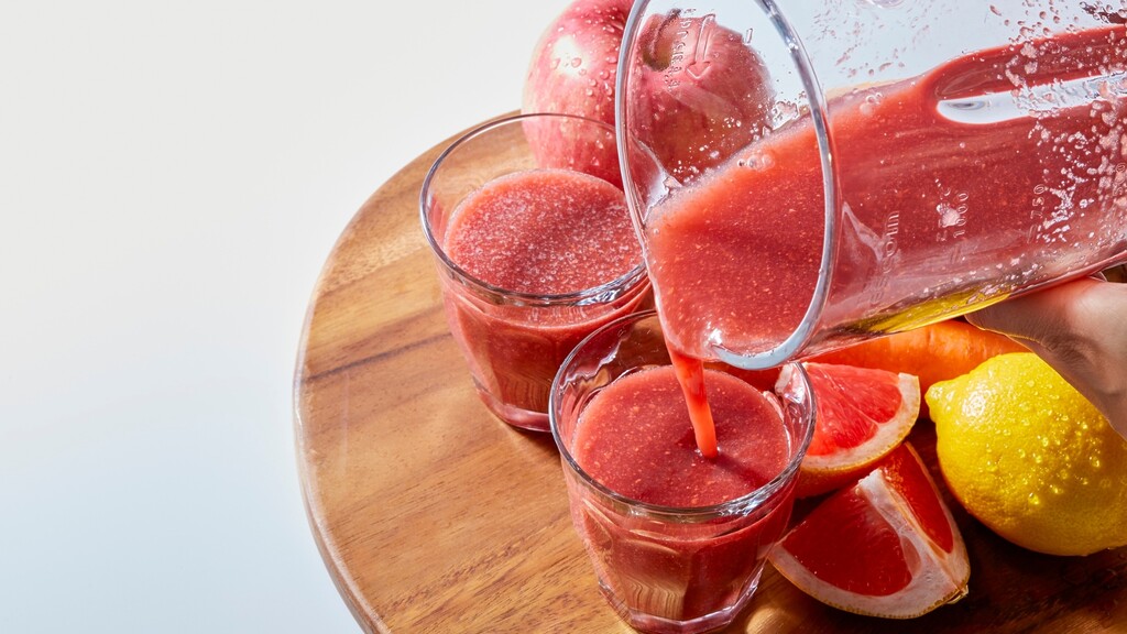 Fresh vitamin C drink being poured into glasses with grapefruit, lemon, and fruit nearby.