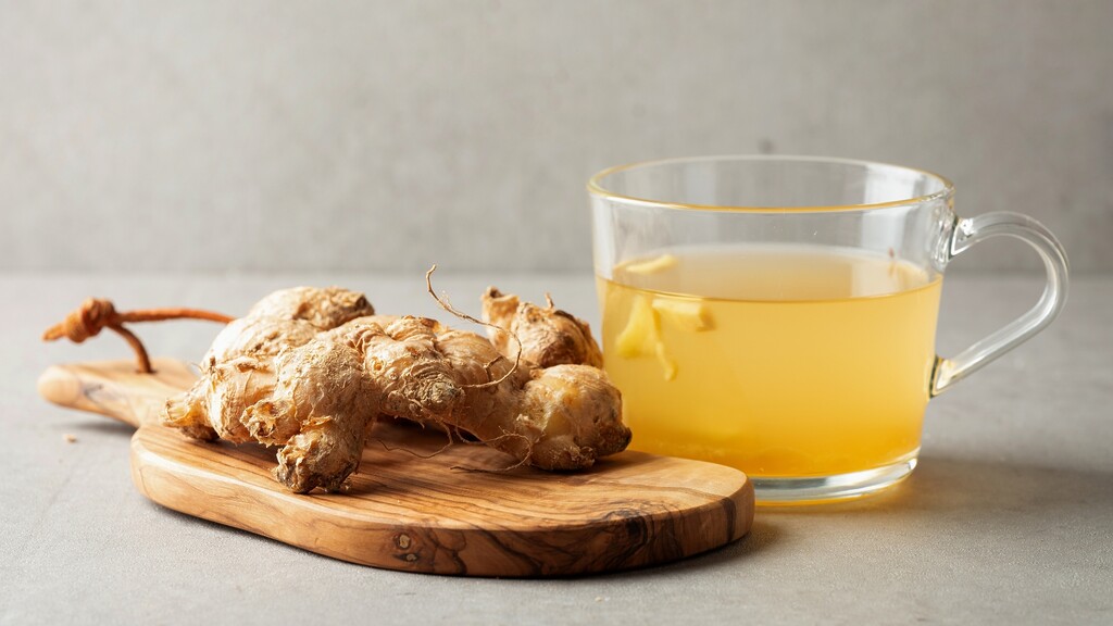 Warm ginger tea in a glass mug beside fresh ginger root on a wooden board.