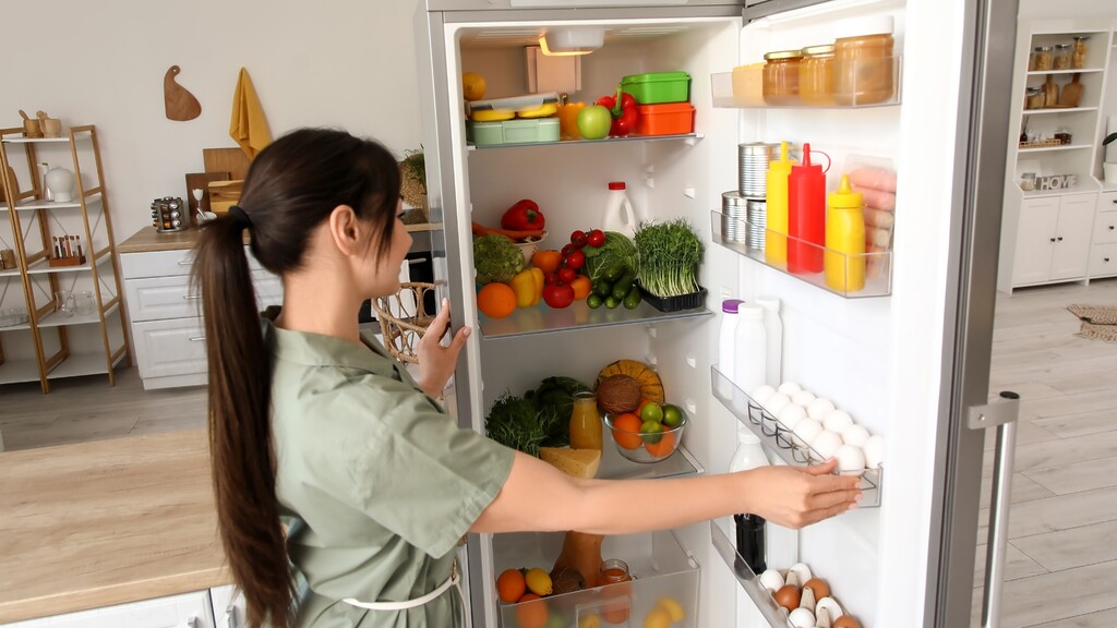 Woman organizing a fridge with eggs, dairy, fruits, vegetables, and healthy foods.
