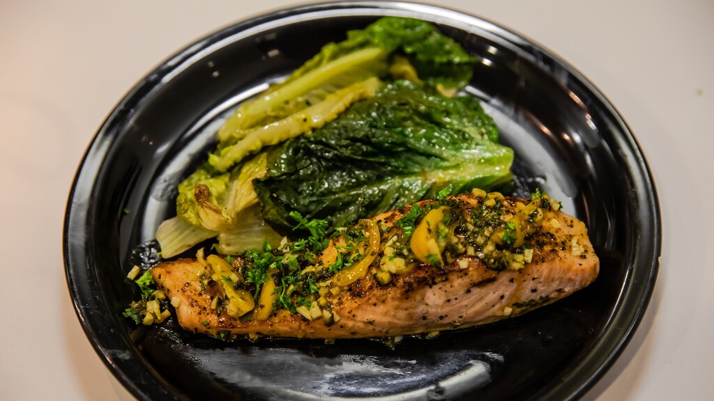 Seared salmon fillet served with leafy greens on a black plate.