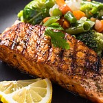 Grilled salmon served with mixed vegetables and lemon on a black plate.