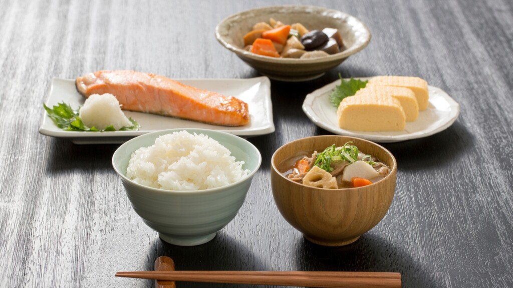 Traditional Japanese meal with rice, soup, grilled salmon, tamagoyaki, and vegetable side dishes.
