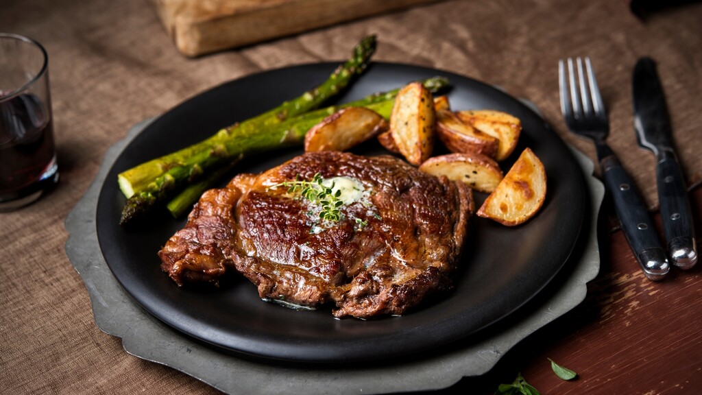 Steak served with roasted potatoes and asparagus on a black dinner plate.