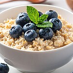 Creamy breakfast porridge topped with blueberries and fresh mint in a white bowl.