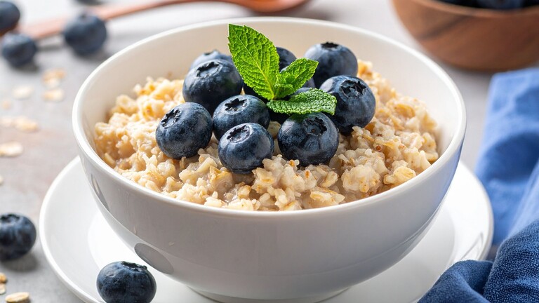 Creamy breakfast porridge topped with blueberries and fresh mint in a white bowl.