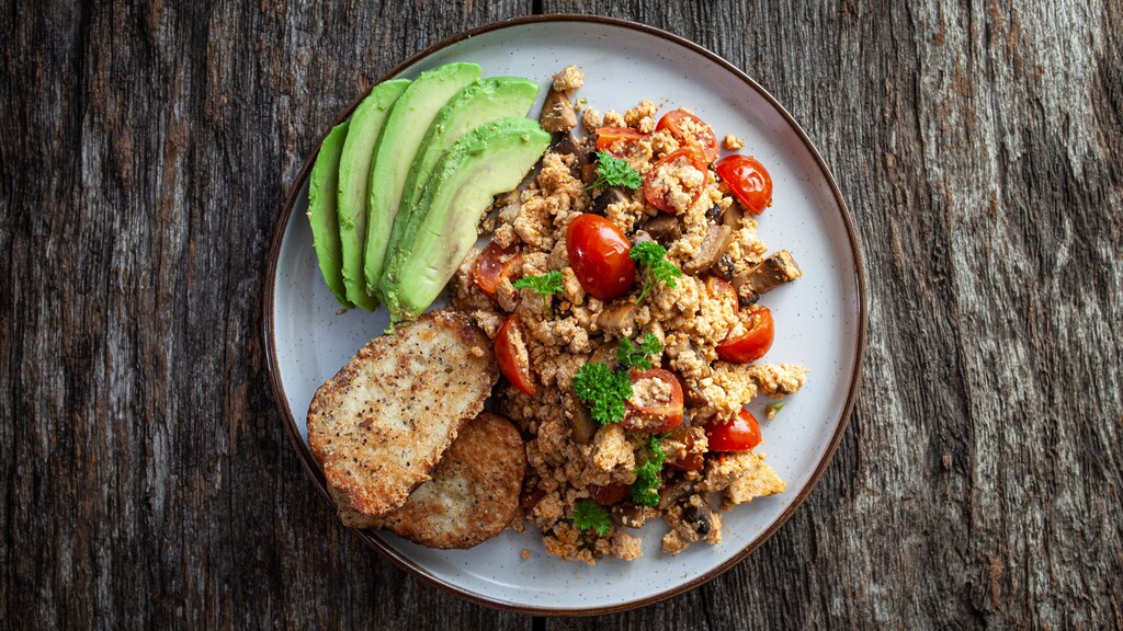 Plant-based breakfast plate with tofu scramble, avocado slices, tomatoes, and crispy patties.