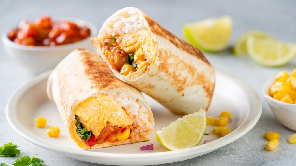 Breakfast burritos filled with scrambled eggs, rice, corn, and salsa, served with lime wedges and cilantro.