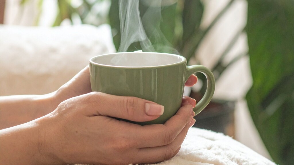 Hands holding a steaming green tea mug during a quiet afternoon tea break.
