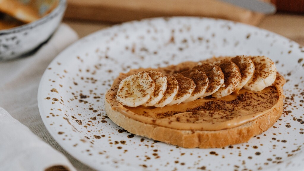 Toast topped with peanut butter, banana slices, and cinnamon on a white plate.