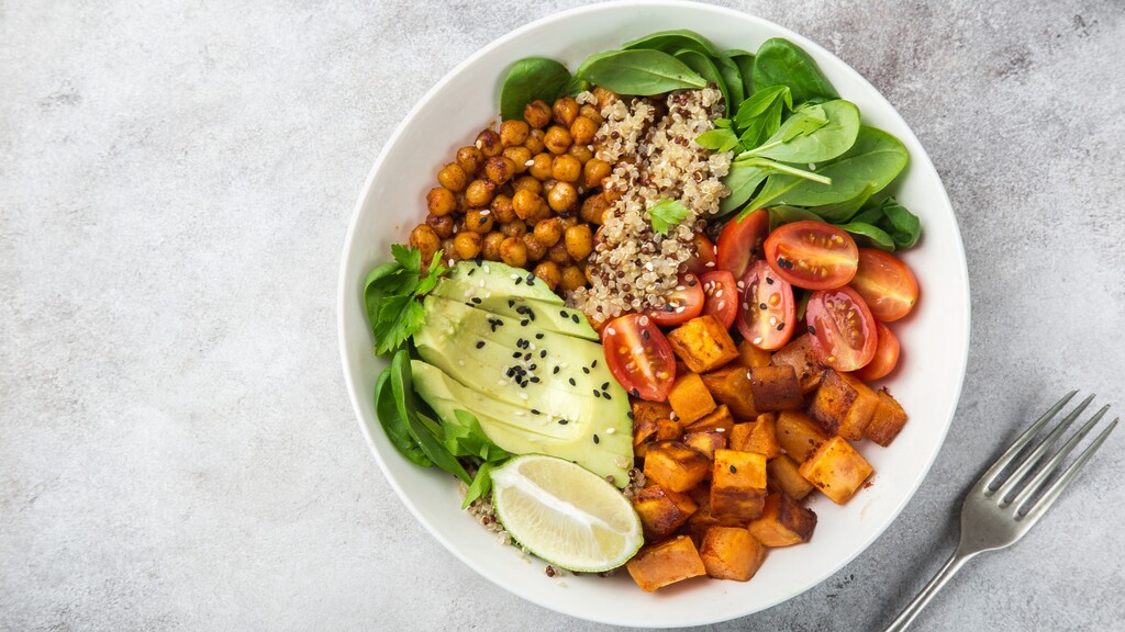 Nourishing quinoa bowl with chickpeas, sweet potatoes, avocado, spinach, and tomatoes.