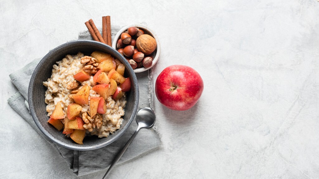 Warm oatmeal bowl topped with apples and walnuts, served with nuts and a fresh apple.