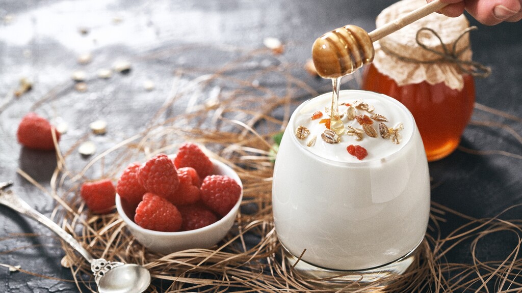 Greek yogurt topped with honey, oats, and raspberries on a rustic breakfast table.