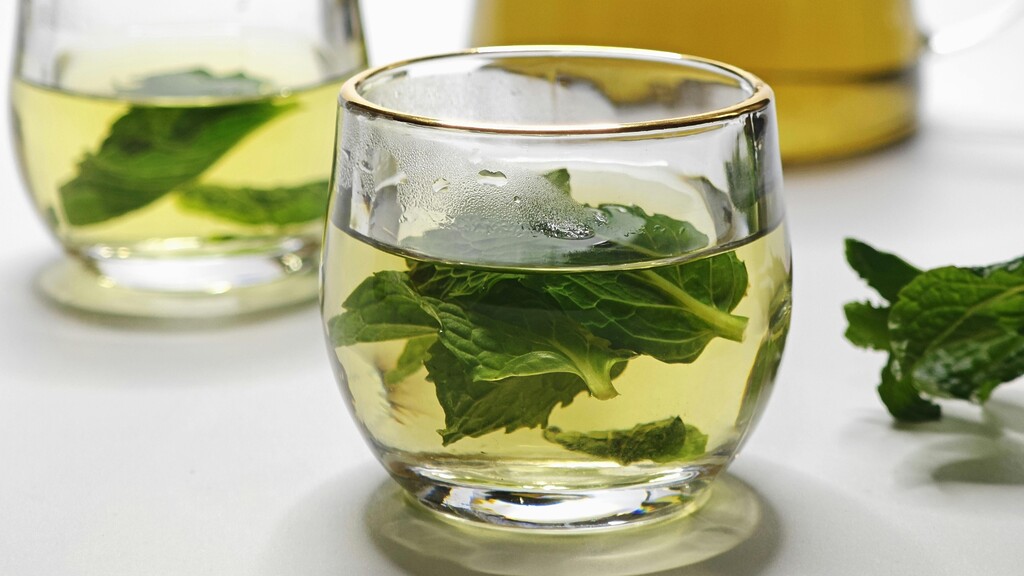 Glass of mint tea with fresh mint leaves on a bright kitchen table.