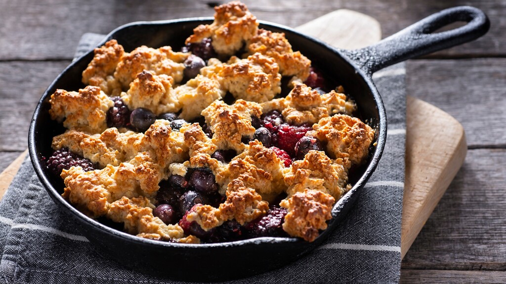 Berry breakfast cobbler baked in a cast iron skillet on a wooden table.
