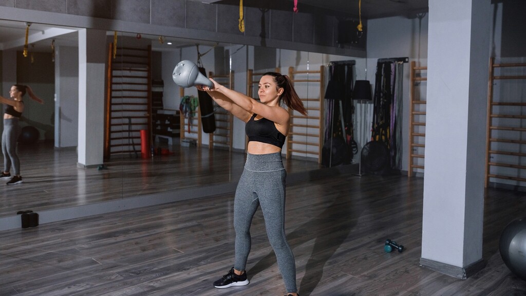 Woman performing a kettlebell swing in a gym during a strength workout.