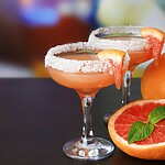 Two grapefruit Paloma cocktails with salted rims, citrus wedges, fresh mint, and whole grapefruit on a bar.
