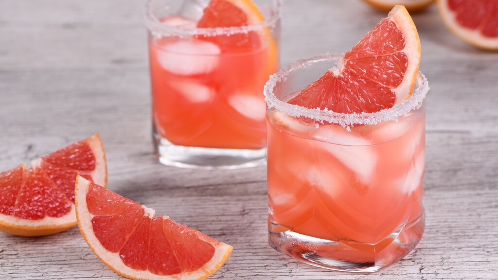 Grapefruit Paloma cocktail over ice with a salted rim and fresh grapefruit wedges on a wooden table.