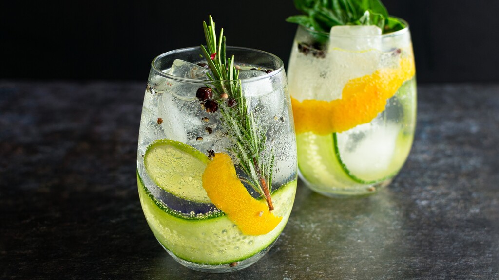 Cucumber basil gin cocktails with citrus peel, herbs, ice, and sparkling water in stemless glasses.
