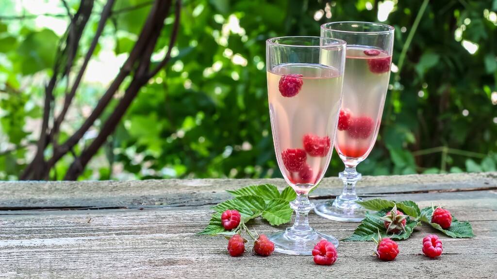 Sparkling berry spritz with raspberries in flute glasses on a rustic outdoor table.
