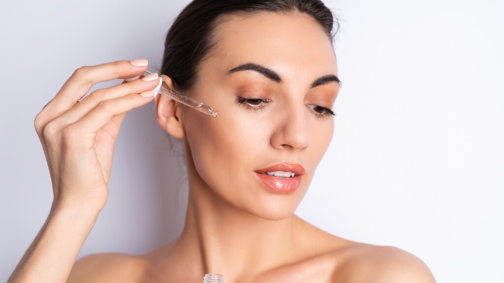 Woman applying facial serum with a dropper as part of an anti-aging skincare routine.