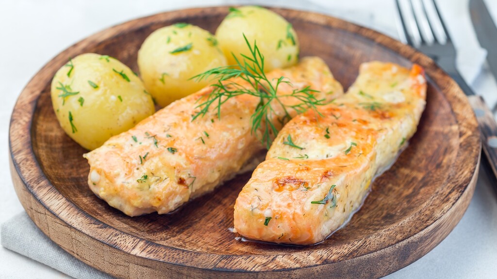 Baked salmon fillets served with boiled potatoes and fresh dill on a wooden plate.