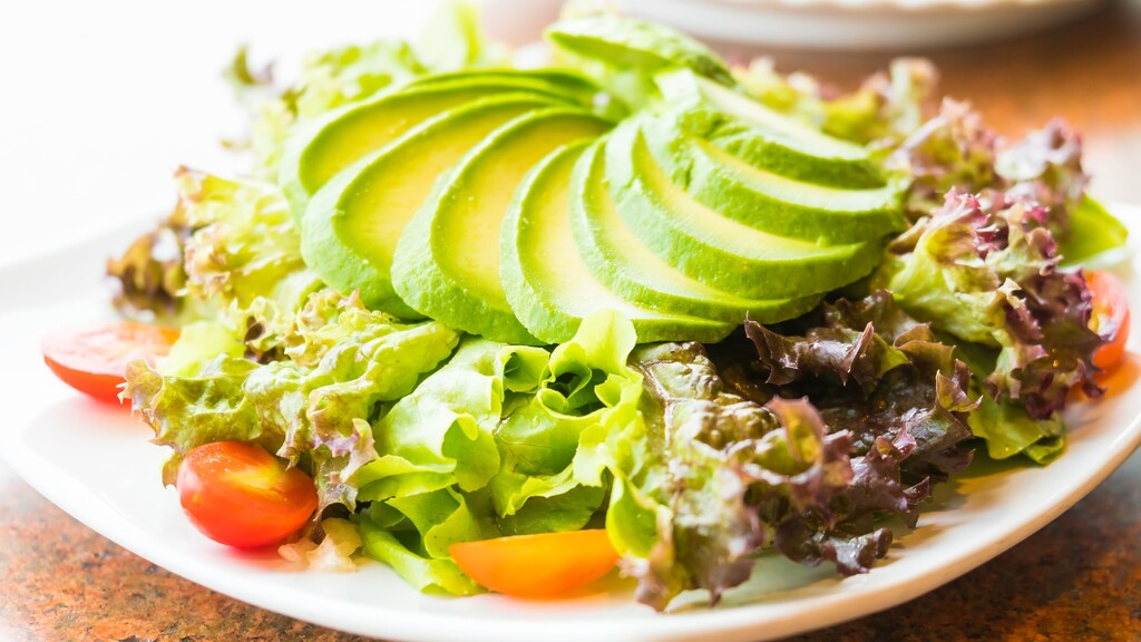 Fresh green salad topped with sliced avocado, lettuce, and cherry tomatoes.