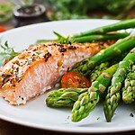 Grilled salmon with asparagus and cherry tomatoes on a white plate for a balanced low-carb meal.