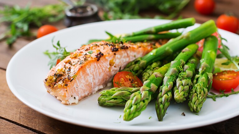 Grilled salmon with asparagus and cherry tomatoes on a white plate for a balanced low-carb meal.