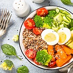 Balanced grain bowl with boiled egg, avocado, broccoli, carrots, tomatoes, and spinach.