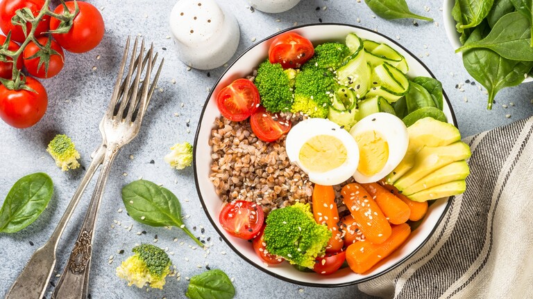 Balanced grain bowl with boiled egg, avocado, broccoli, carrots, tomatoes, and spinach.