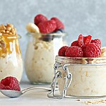 21 Day Fix Overnight Oats: Easy Make-Ahead Breakfast Recipes Three jars of overnight oats topped with raspberries, banana, walnuts, and honey on a light kitchen surface.