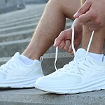 15 Reasons to Lace Up Your Sneakers Today Man tying the laces of white walking shoes while sitting on outdoor steps before a walk.