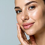 Woman with glowing skin touching her face after a simple skincare routine.