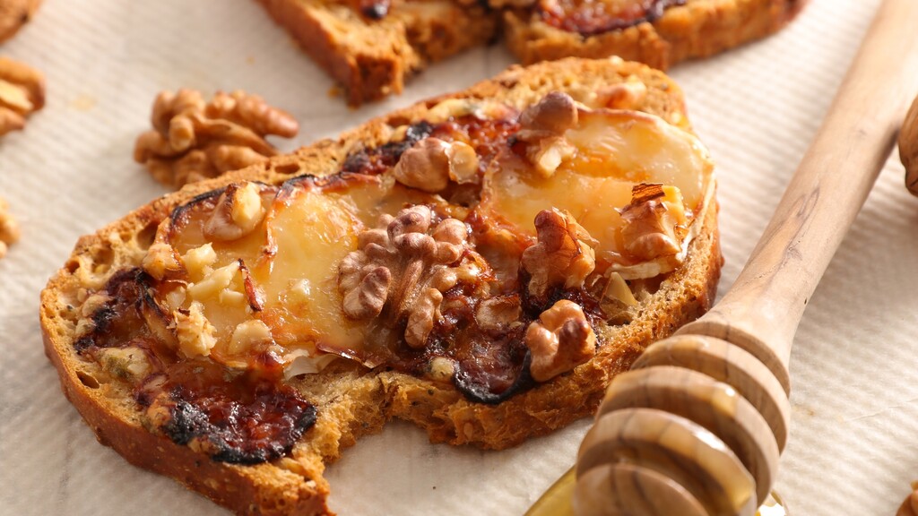 Walnut-topped toast with melted cheese and honey on a warm rustic surface.