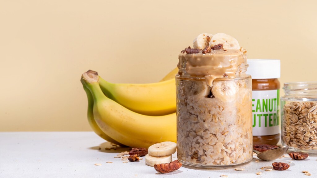 Peanut butter banana overnight oats in a jar with sliced bananas, oats, pecans, and peanut butter nearby.