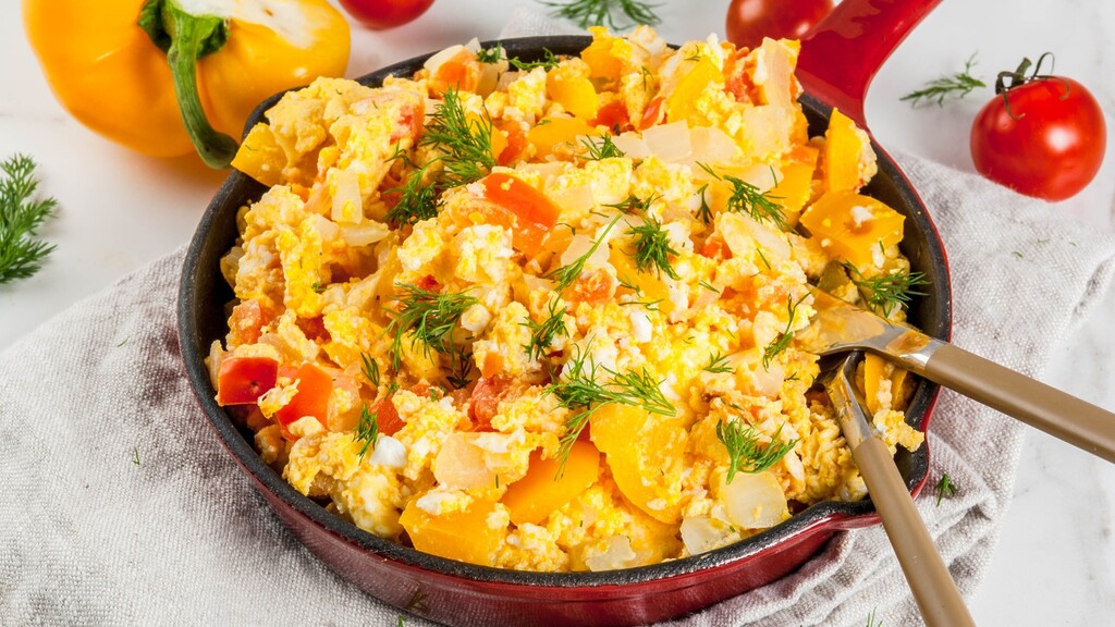 Scrambled eggs with yellow bell pepper, tomatoes, onion, and fresh dill served in a skillet.