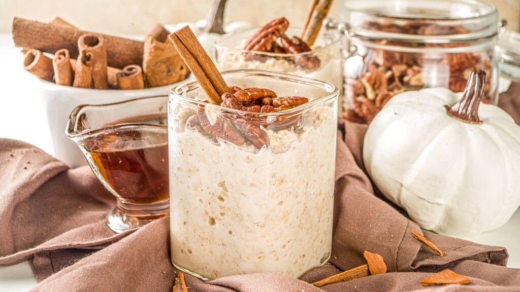 Pumpkin spice overnight oats topped with pecans and cinnamon, served with maple syrup and fall ingredients.