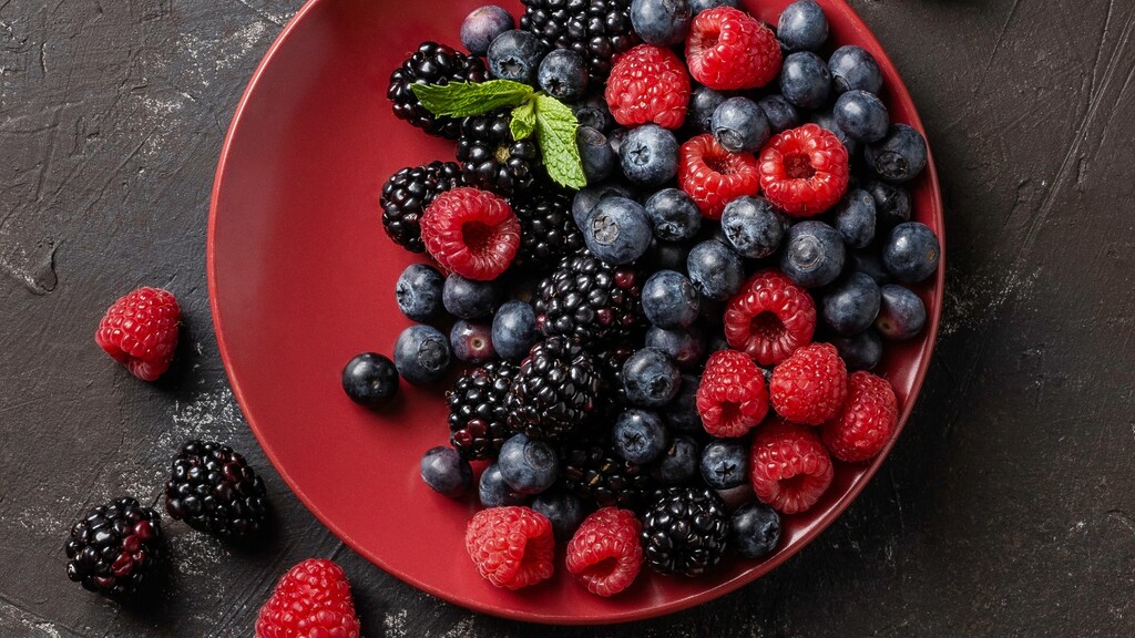 Mixed raspberries, blueberries, and blackberries served in a red bowl.