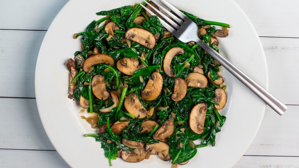 Sautéed spinach with mushrooms served on a white plate.